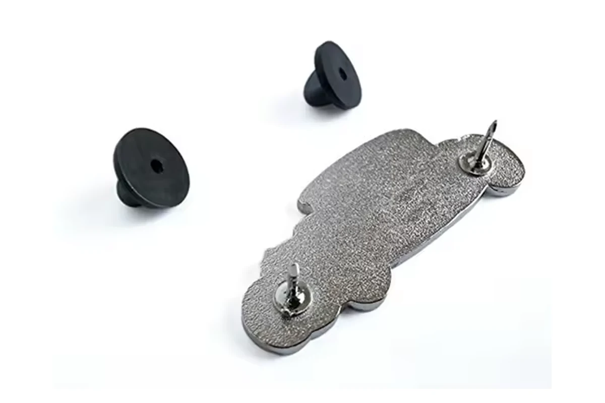 Dark textured back of a vehicle-shaped pin with two posts and two detached rubber clutches.