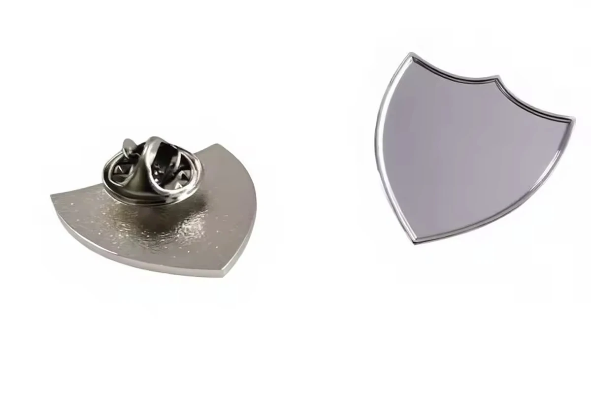 A silver shield-shaped blank pin shown from the front and back, with a metal butterfly clutch.