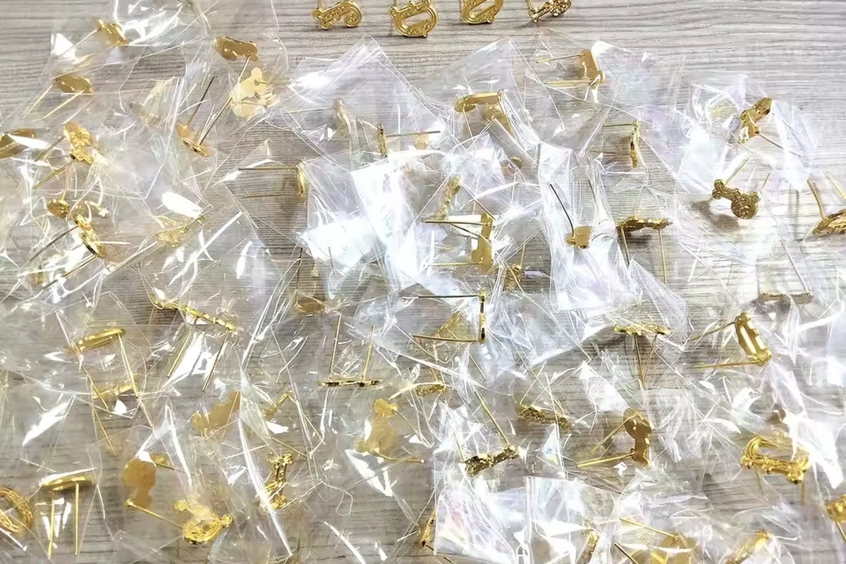 Small gold-tone shaped pins or pin components in many individual clear plastic bags.