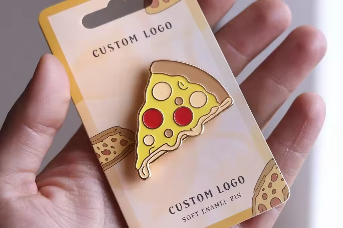 Pizza-slice pin mounted on a printed backing card held in a hand.
