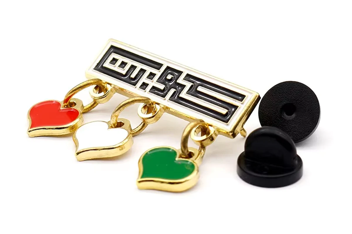 Letter-shaped pin with three heart charms beside black rubber clutches.