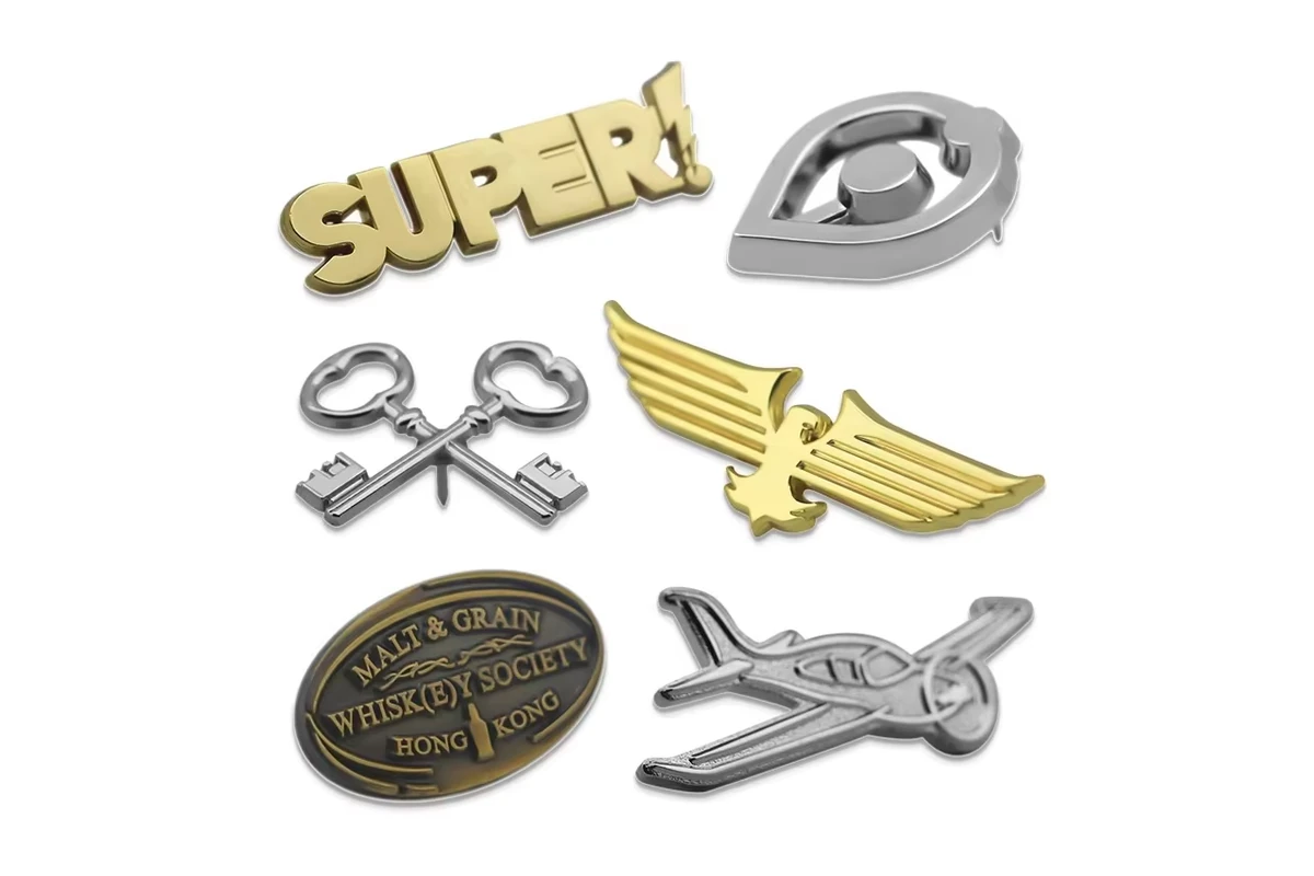 Gold and silver metal pins in word, wing, key, oval and aircraft shapes.