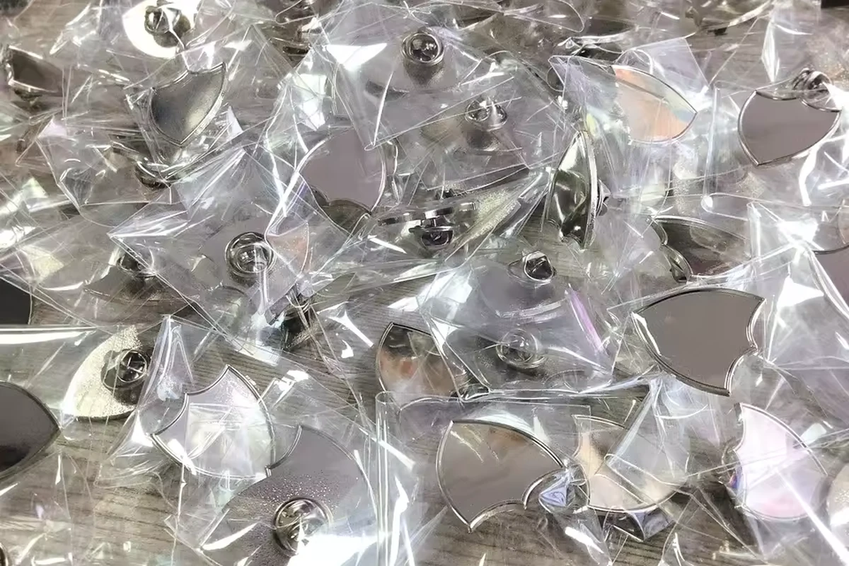 A batch of silver shield-shaped pins individually packed in clear plastic bags.