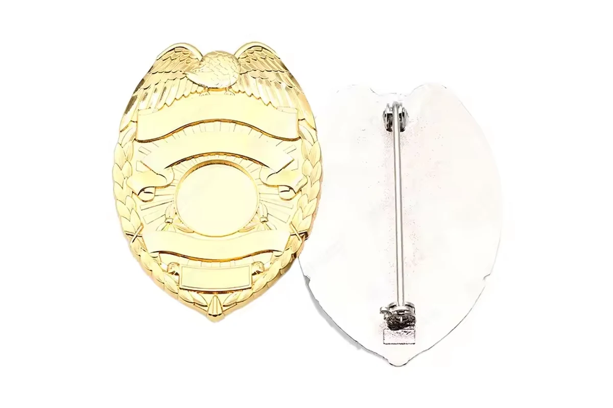 Gold unfilled shield badge shown front and back with a safety-pin fastening.