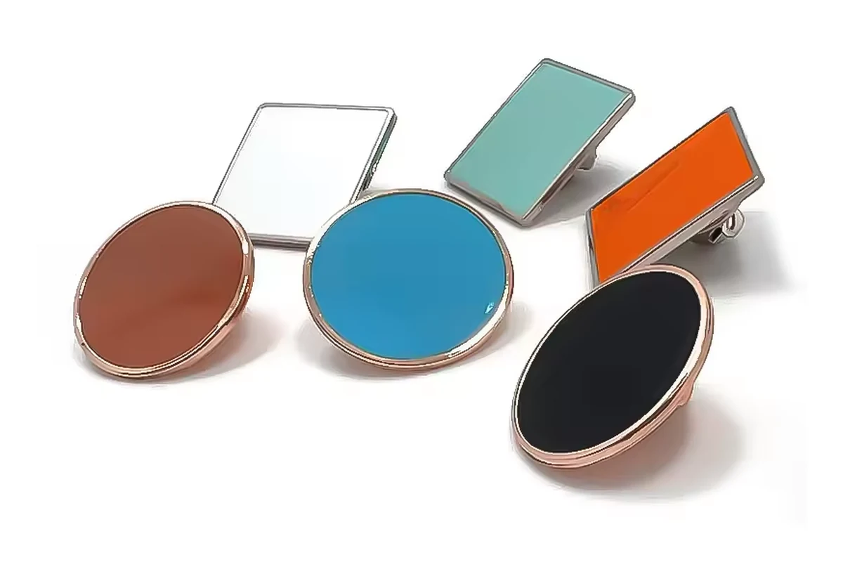 Assorted blank colored pin faces in round, square, rectangular and oval metal settings.