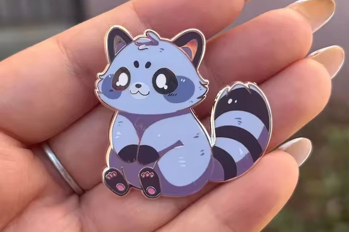 A raccoon pin resting on a hand.