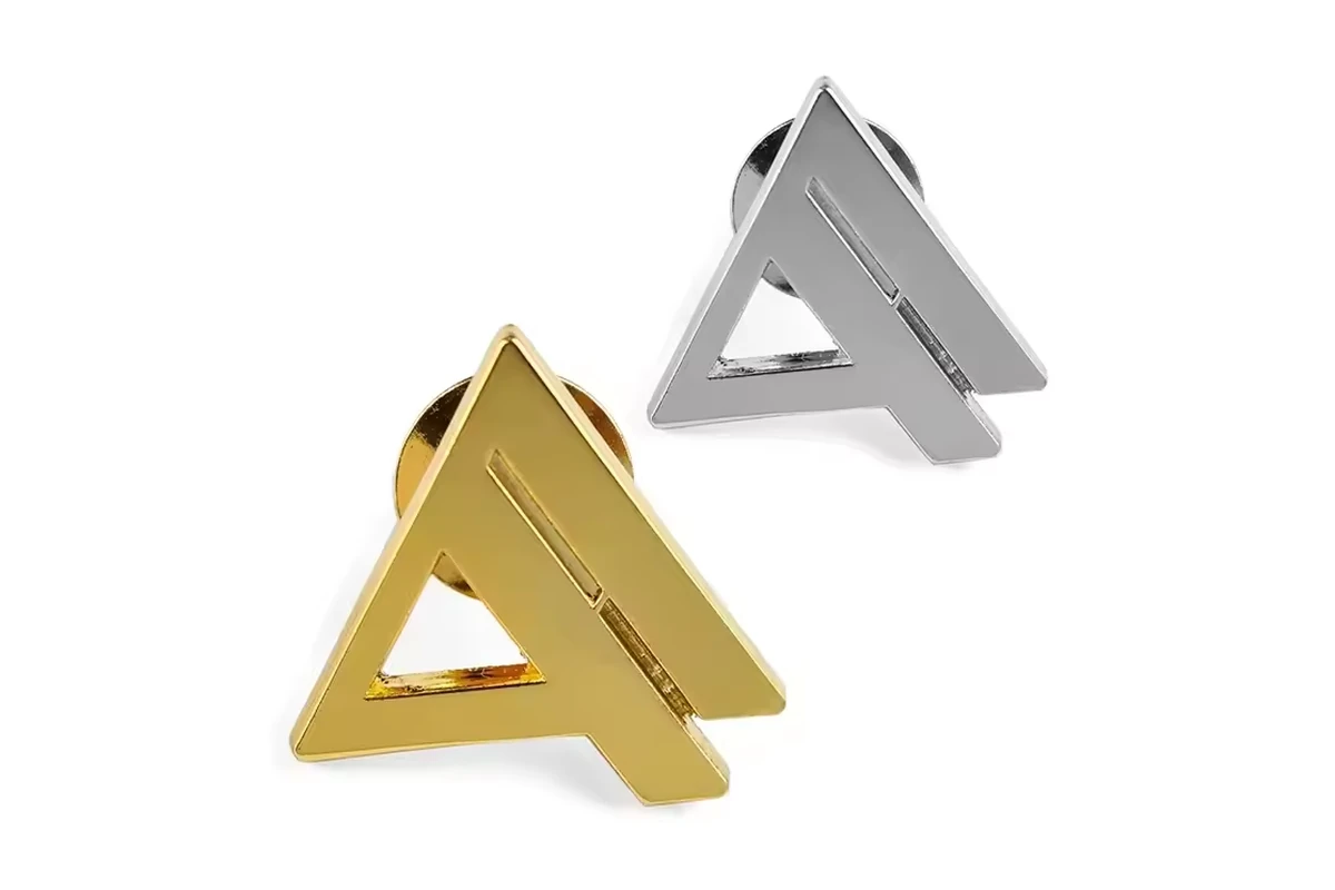Two triangular cutout metal pins in gold-colored and silver-colored finishes on white.