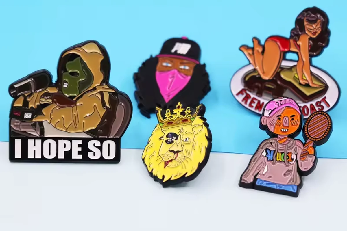 Five colorful character and animal enamel pins arranged against a blue background.