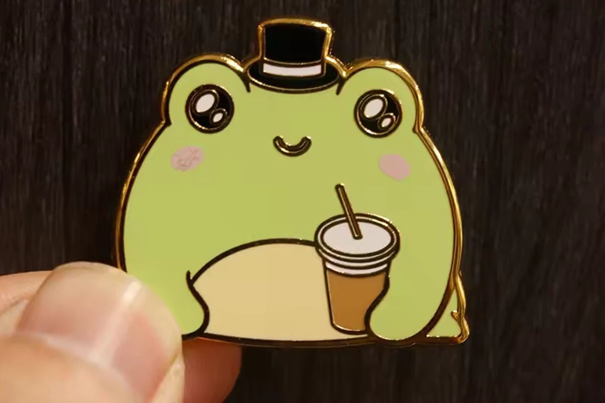 A hand holding a green frog pin.