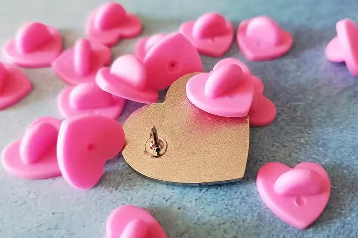 Pink heart-shaped rubber clutches surrounding a gold-tone pin back with a visible post.