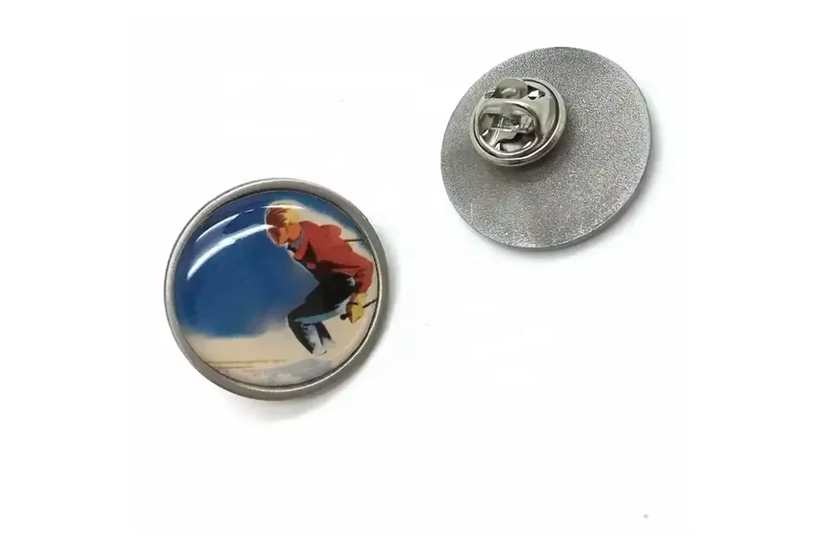 A domed round surfer-photo pin beside its silver reverse with a butterfly clutch.