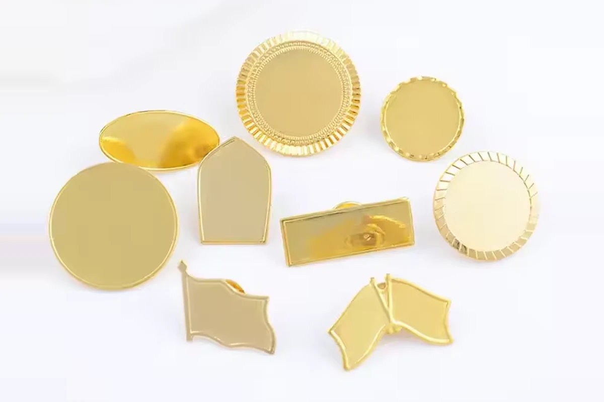 Gold-colored blank metal badge bases in round, rectangular, shield and flag shapes.