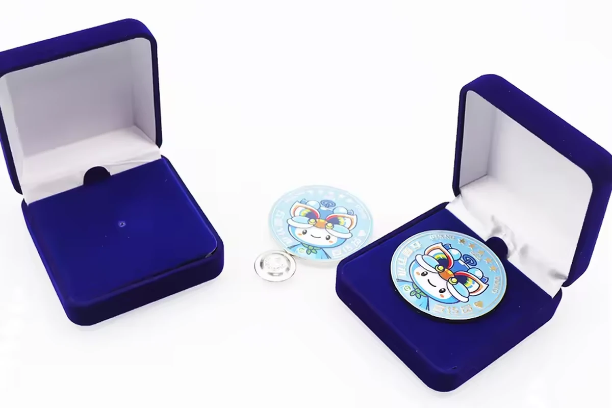Two open blue velvet presentation boxes with round illustrated badges and a small silver attachment.