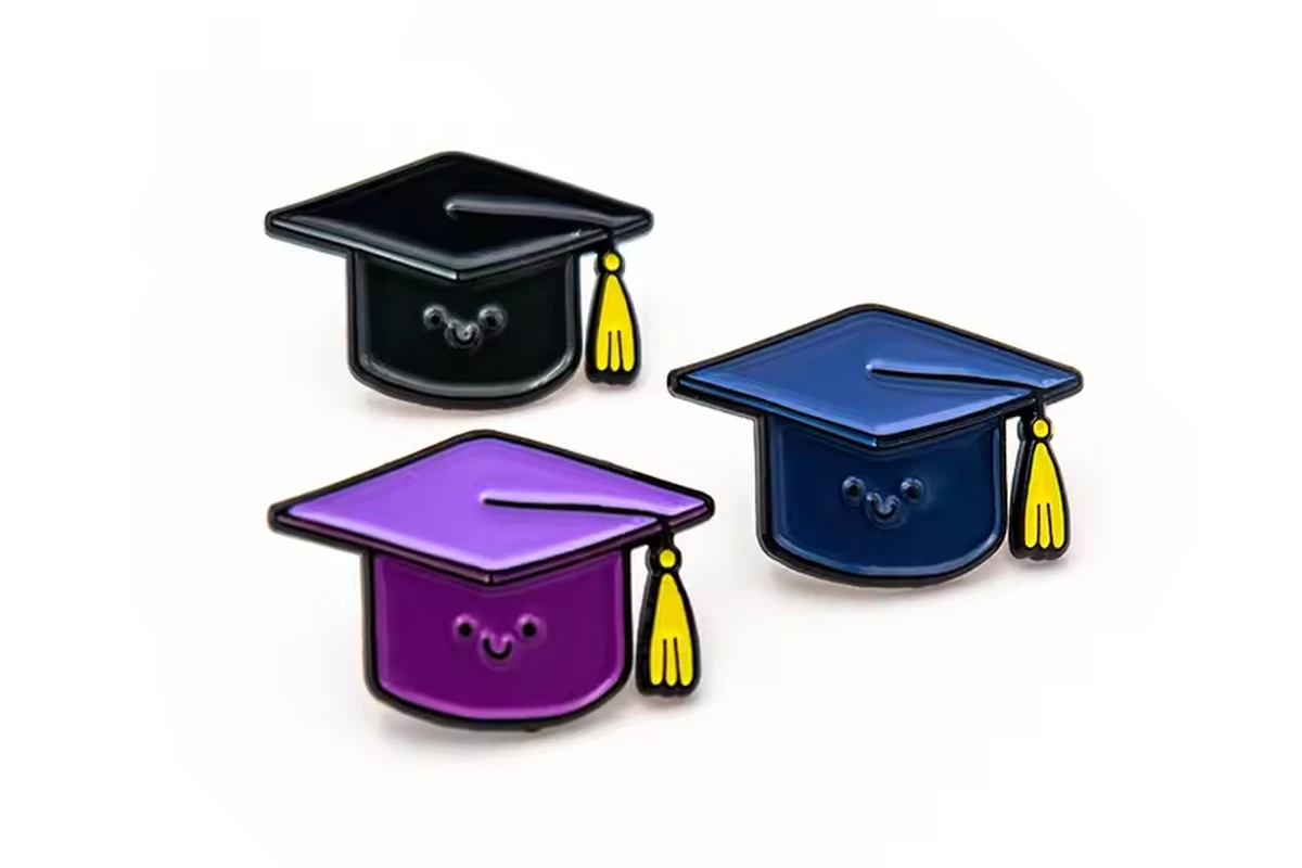 Three graduation-cap pins in black, blue and purple with yellow tassels on a white background.
