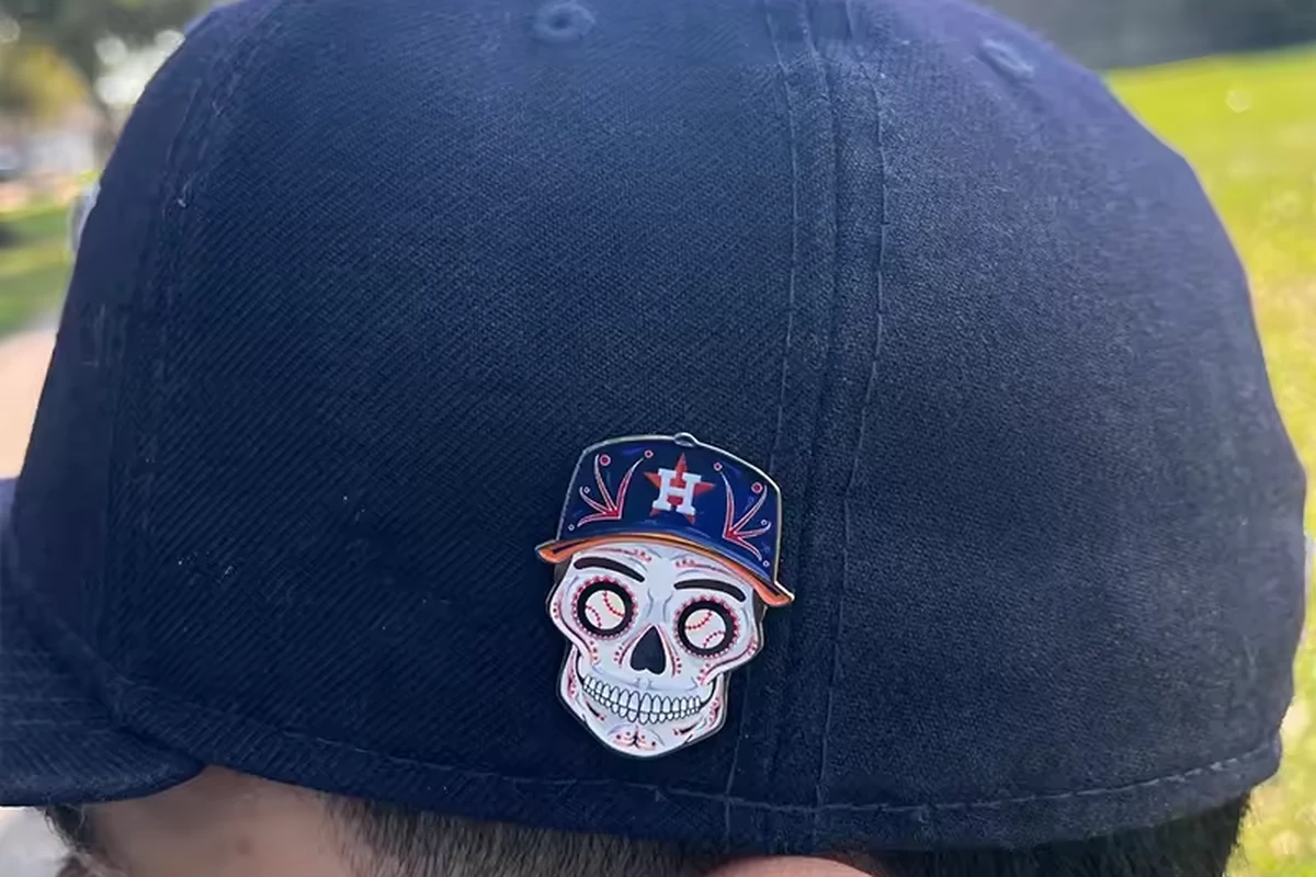 Small embroidered-look skull team pin worn on a navy baseball cap outdoors.