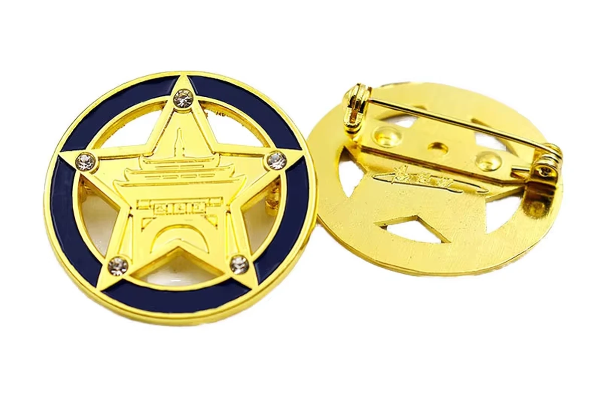 A gold-colored circular star badge with a dark blue ring beside its reverse with a safety-pin fitting.