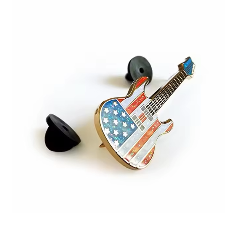 Angled view of an American flag guitar pin beside two black rubber pin backs.