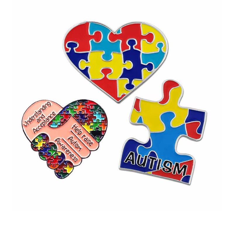 Three autism awareness pins featuring a puzzle heart, a handshake and a puzzle piece with AUTISM lettering.