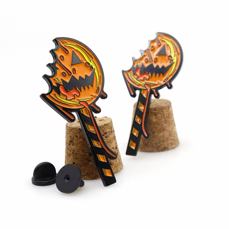 Two bitten pumpkin lollipop pins with orange jack-o-lantern faces and black striped sticks, displayed on cork stands beside black pin backs.