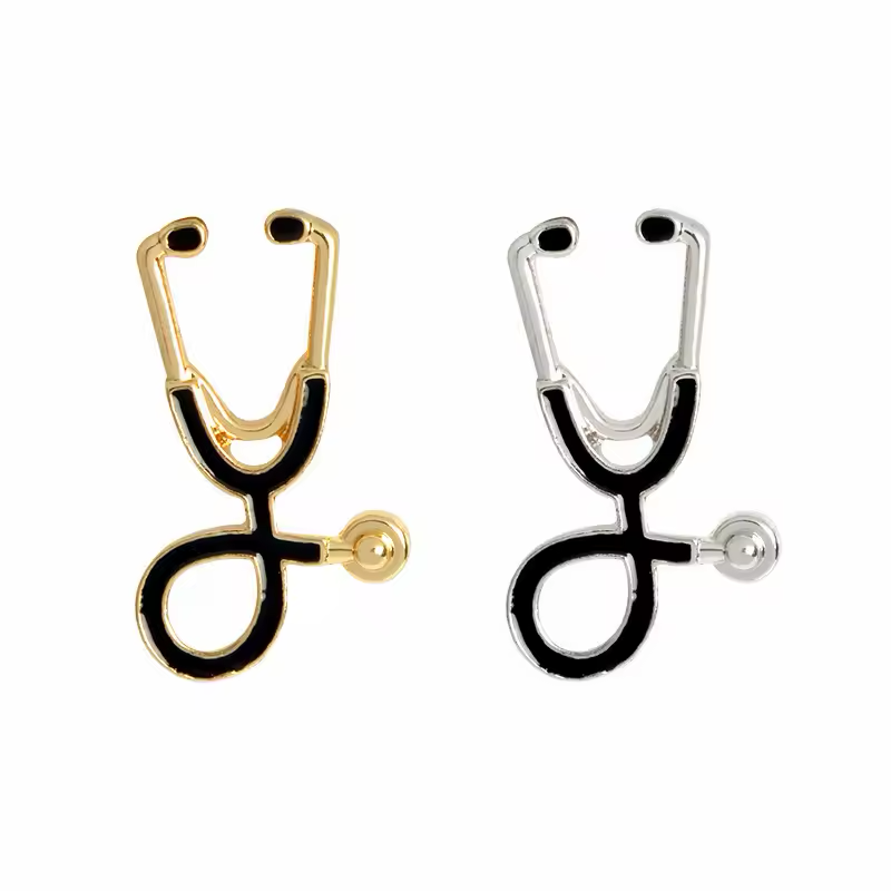Two black stethoscope-shaped pins with gold-tone and silver-tone outlines on a white background.