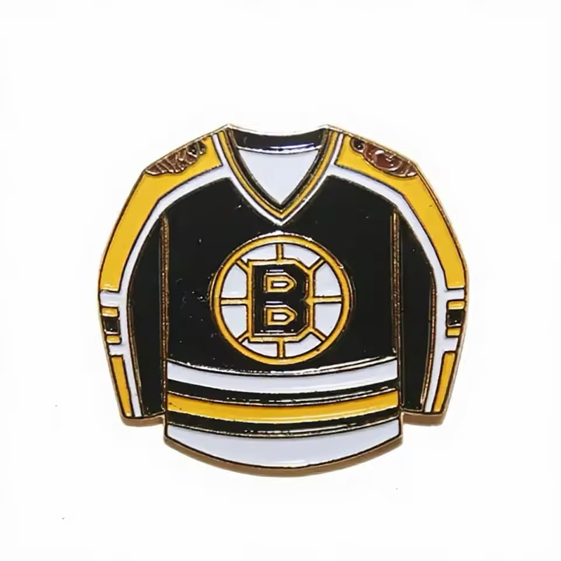 Black hockey jersey-shaped pin with yellow and white stripes, a circular B emblem on the chest and gold-tone outlines on a white background.