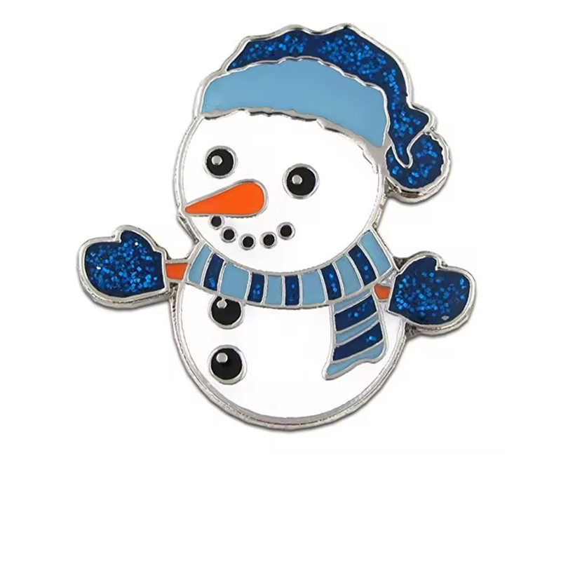 White snowman pin with a blue glitter hat and mittens, a striped blue scarf, an orange carrot nose, black buttons and silver-tone outlines on a white background.