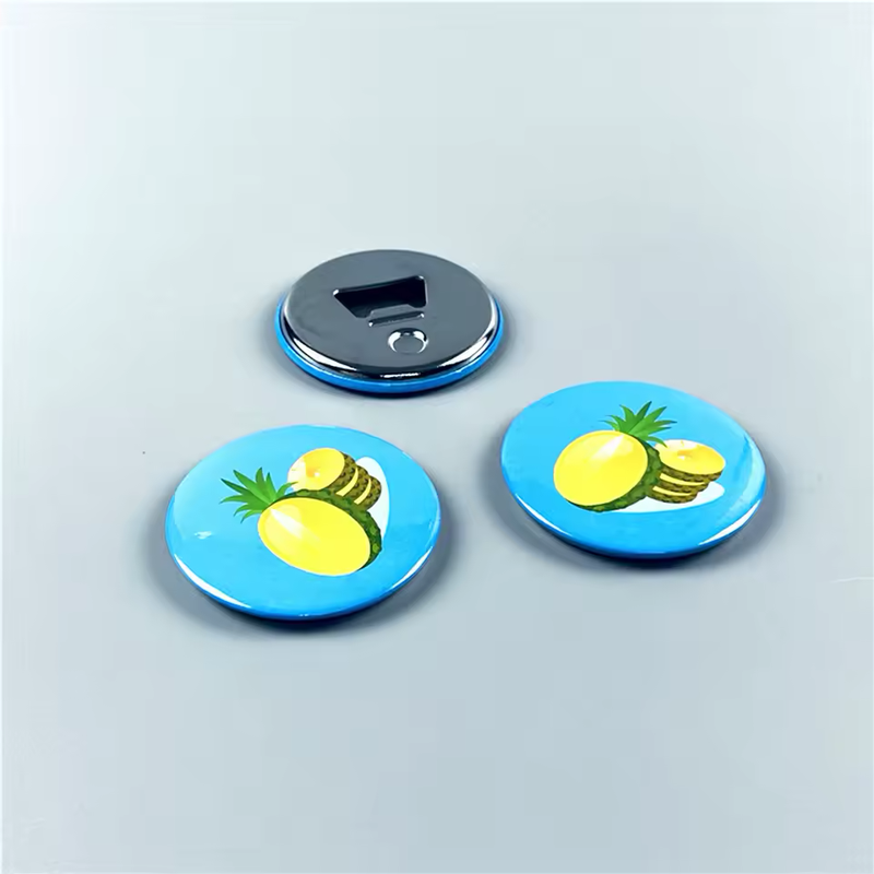Three round button-style bottle openers on a pale blue-gray surface, with two blue pineapple designs facing up and one silver-tone opener back visible.