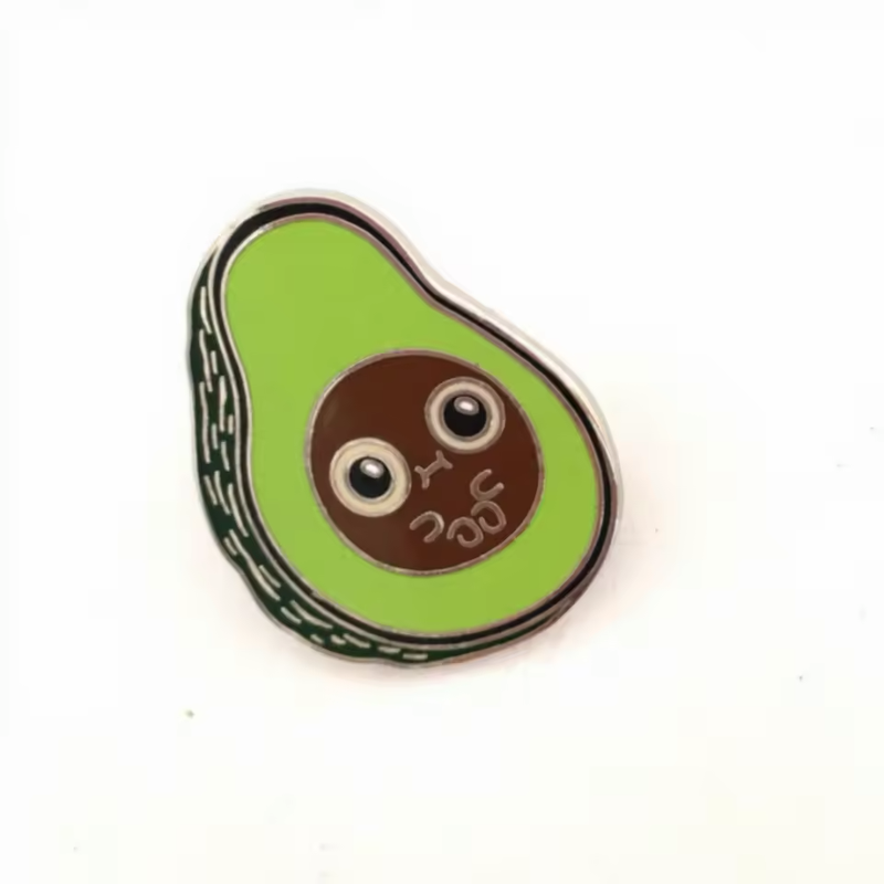 Green avocado half pin with a brown pit, large round eyes and a small cartoon face on a white background.