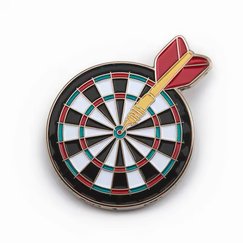 Round black and white dartboard pin with red and teal scoring rings and a gold-tone dart with red flights hitting the bullseye on a white background.
