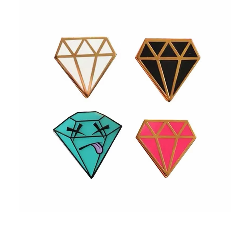Four diamond-shaped pins in white, black and pink with gold-tone geometric outlines, and turquoise with black crossed eyes and a purple tongue, on a white background.