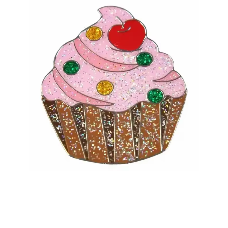 Glitter cupcake pin with pink swirled frosting, a red cherry, green and gold dots and a brown striped wrapper.