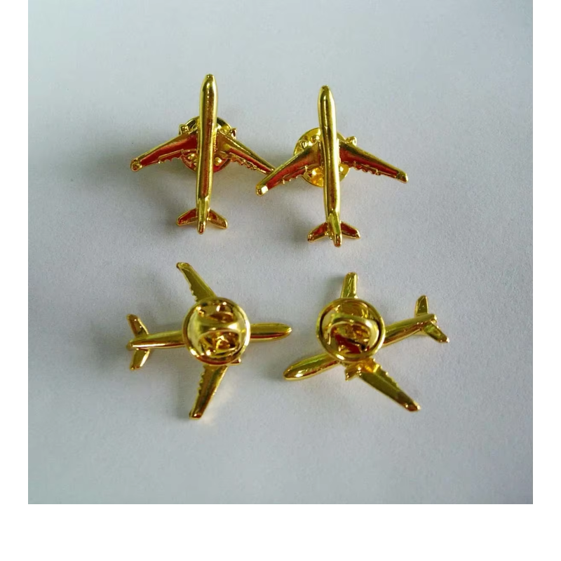 Four gold-tone airplane pins with red accents, showing two front views and two backs with butterfly clutches on a pale fabric background.