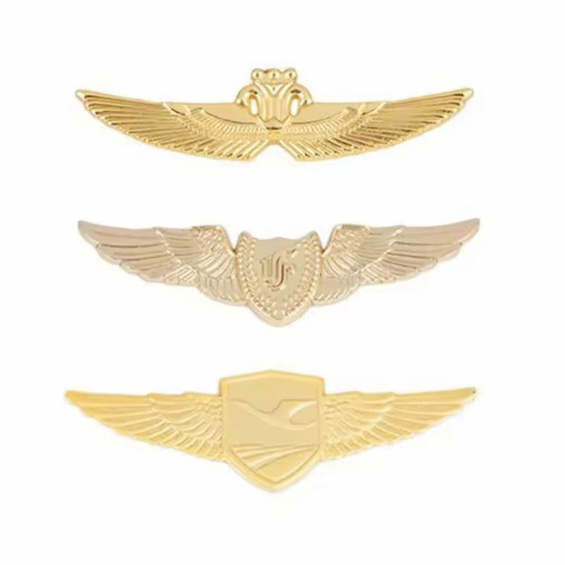 Three gold-tone aviation wing badges with raised feather details and crown or shield center motifs on a white background.