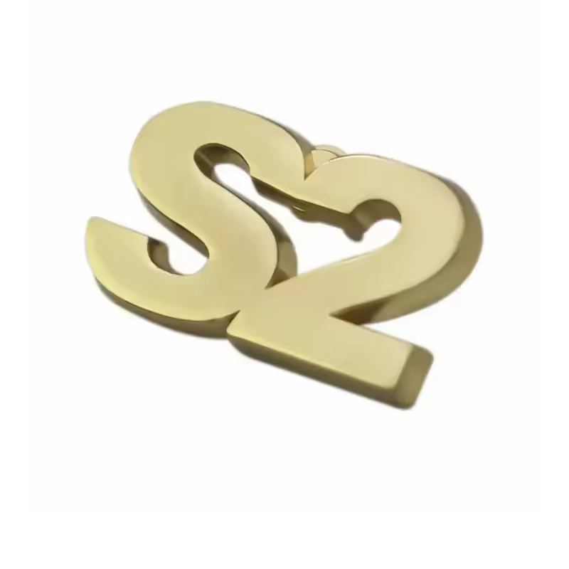 Gold-tone S2 letter and number pin with cutout openings, a smooth reflective face and raised edges, photographed at an angle on a white background.