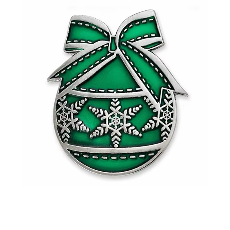 Green Christmas ornament pin with a large bow, silver-tone outlines, snowflake patterns and stitched-line decoration on a white background.