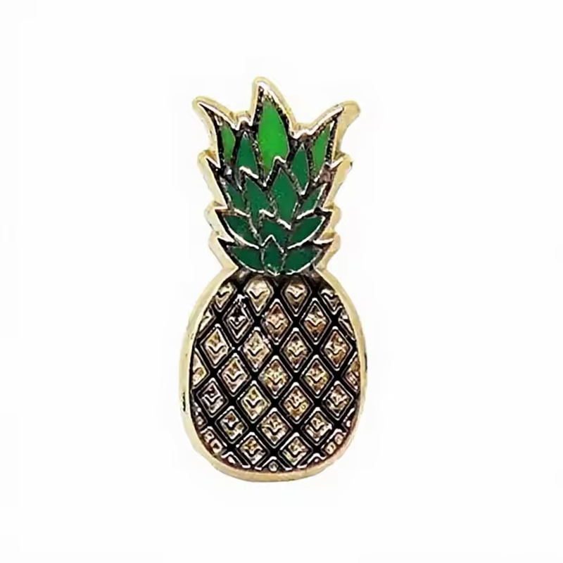 Gold-tone pineapple pin with layered green leaves and a black diamond lattice filled with textured gold-tone details.