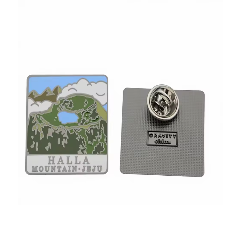 Rectangular Halla Mountain Jeju souvenir pin with a green mountain, blue crater lake, clouds and HALLA MOUNTAIN·JEJU lettering, shown beside its textured back and butterfly clutch on a white background.