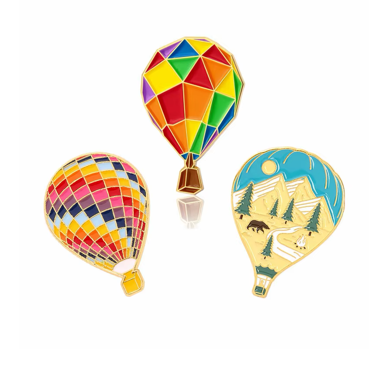 Three hot air balloon pins featuring geometric color blocks, a multicolored grid and a mountain-and-forest scene.