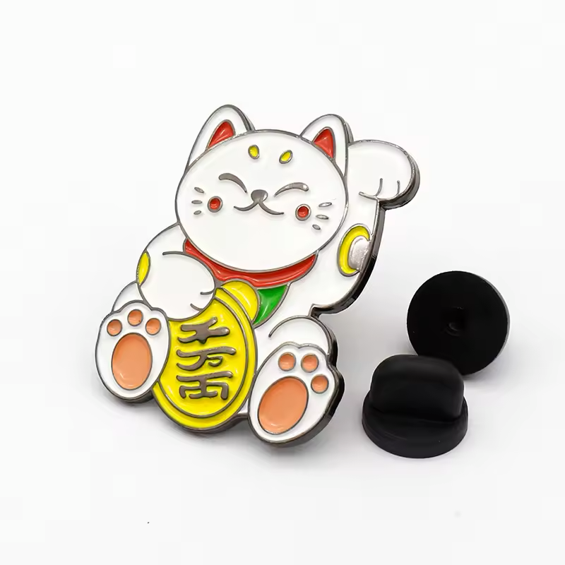 White lucky cat pin holding a gold-colored coin, beside two black pin backs.