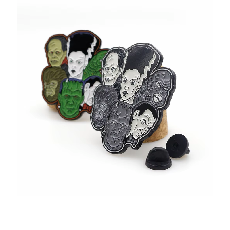 Monster face collage pins in color and black-and-white versions, displayed on cork stands beside black pin backs.