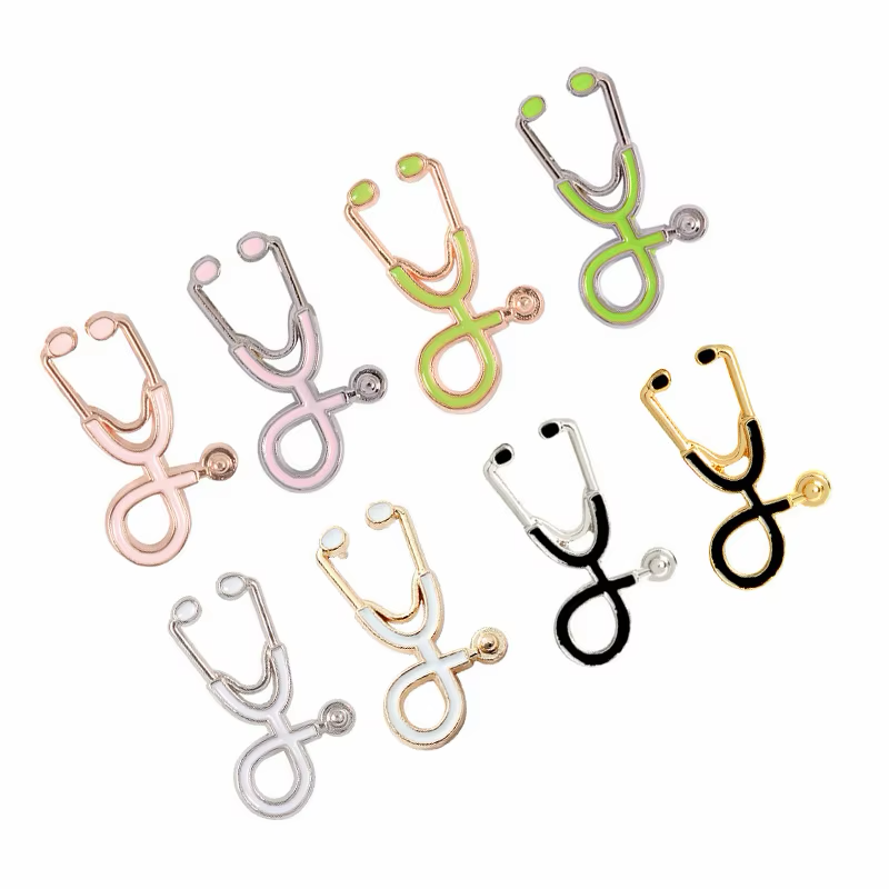 Eight stethoscope-shaped pins in pink, green, white and black with gold-tone, rose-gold-tone and silver-tone outlines on a white background.