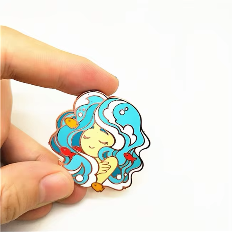 Hand holding a pin with a girl's face, turquoise waves and small fish.