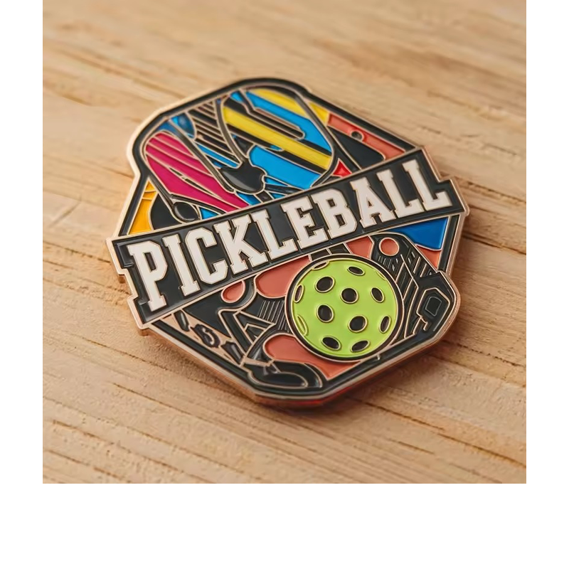 Colorful pickleball pin with paddle shapes, a green perforated ball, bold PICKLEBALL lettering and metal outlines on a wooden background.