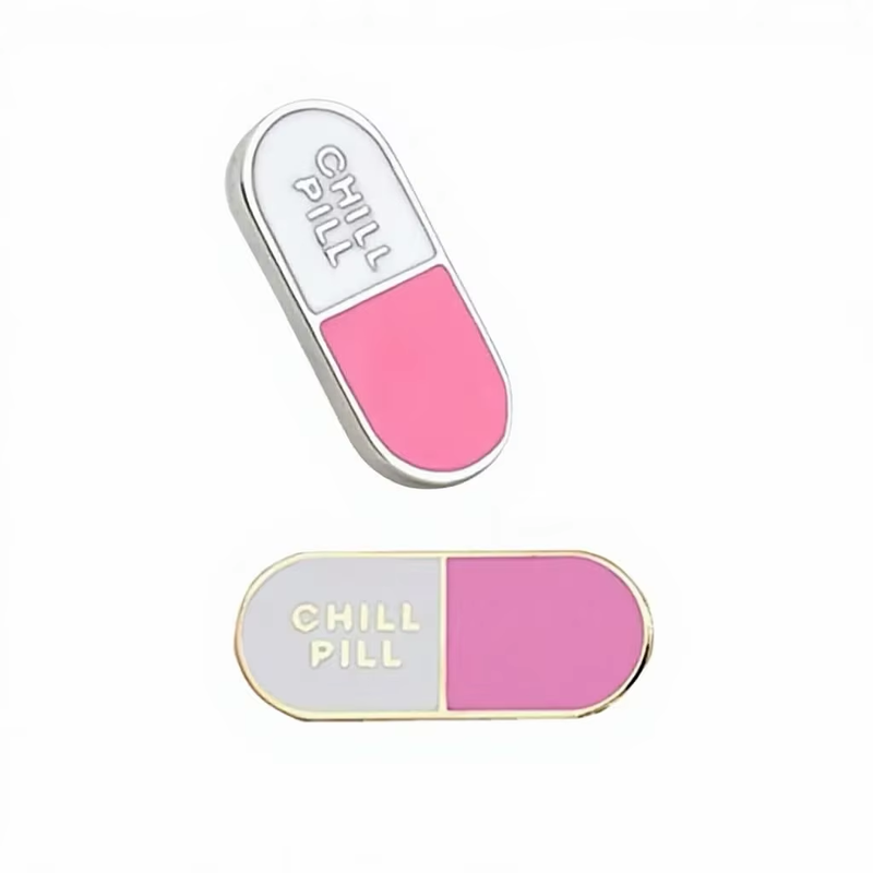Two pink and white capsule-shaped pins with CHILL PILL lettering and silver-tone or gold-tone outlines on a white background.