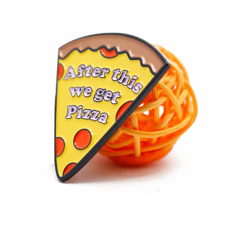 Yellow pizza slice pin with red toppings, brown crust and the words After this we get Pizza, resting against an orange woven ball.