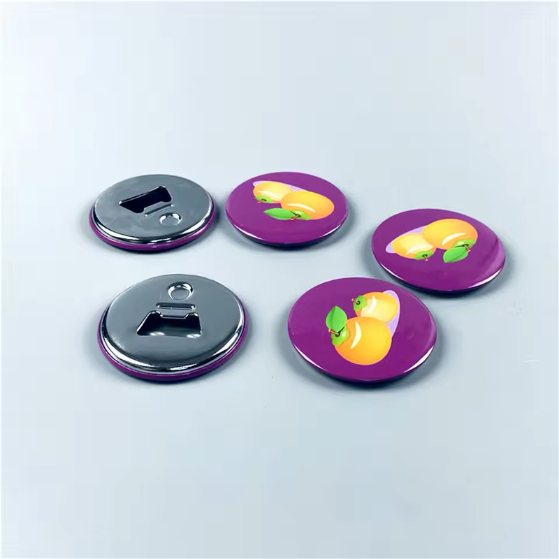 Five round button-style bottle openers on a pale blue-gray surface, with three purple yellow-fruit designs facing up and two silver-tone opener backs visible.