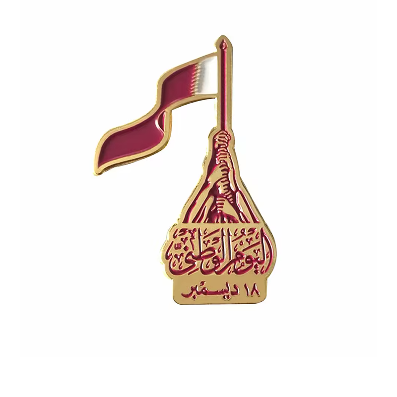 Gold-colored Qatar flag pin with stacked hands holding the flagpole, maroon Arabic lettering and an 18 December date.