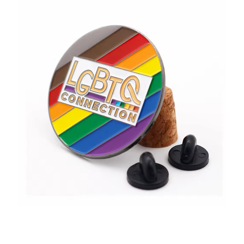 Round rainbow-striped pin marked LGBTQ Connection, displayed on a cork stand beside two black rubber pin backs.