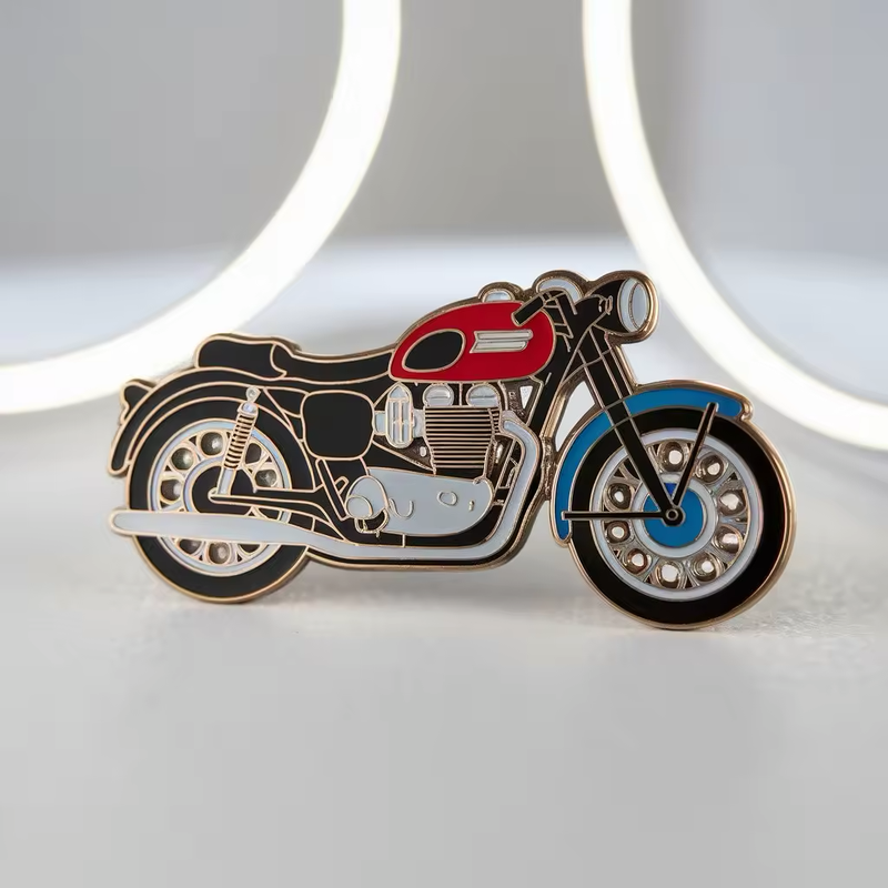 Vintage-style motorcycle pin with a red fuel tank, blue front fender, black seat and tires, silver-tone engine details and gold-tone outlines against a gray background with curved light shapes.
