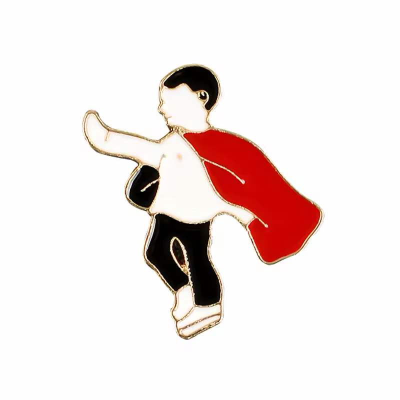 Gold-tone outlined superhero character pin with black hair and trousers, a white shirt and a red cape, posed with one arm extended on a white background.